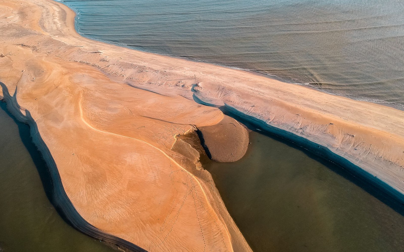 An aerial view of a sand spit with a tidal channel cutting through it