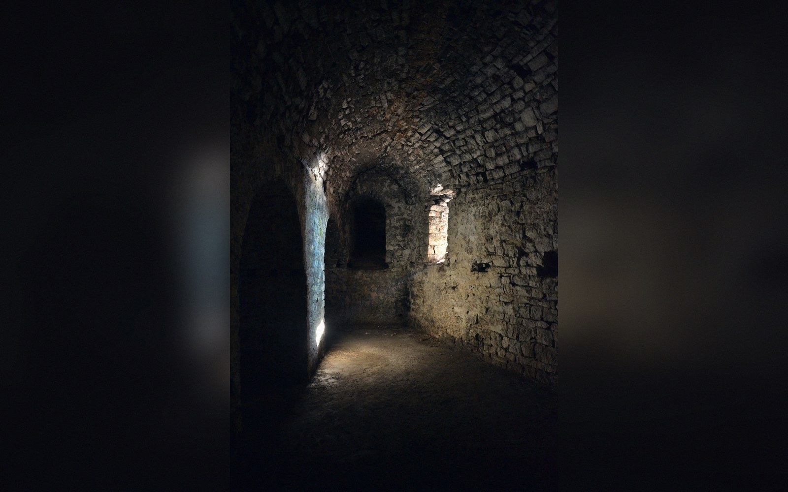 A barrel-vaulted stone corridor inside a coastal fortress, lit by a single embrasure